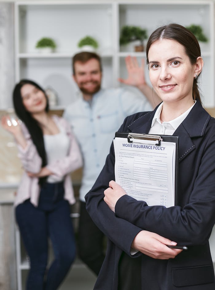 A smiling businesswoman holding a home insurance policy with clients in the background.